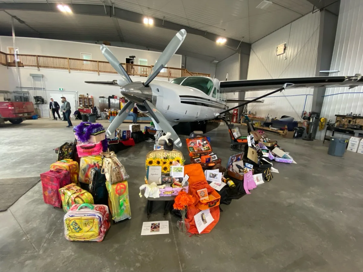 A collection of decorated suitcases created by people at TOZ, displayed in front of a plane at the Tintina hangar, 2023