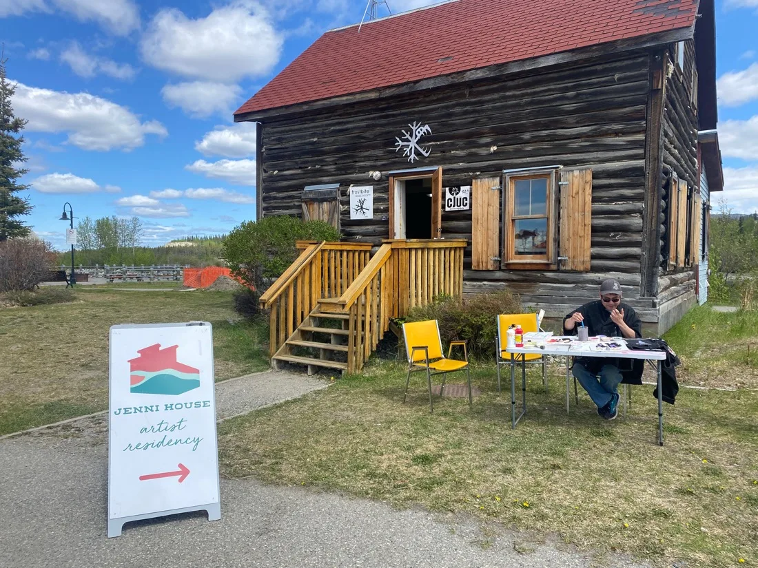 Ernest painting at the outdoor table in front of the Jenni House at Shipyards Park, 2024