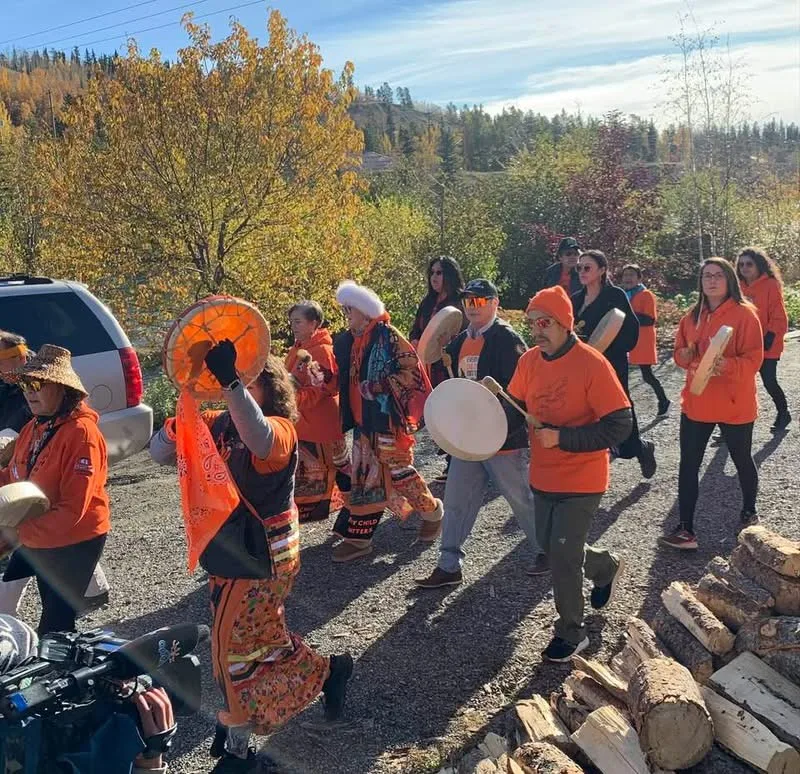 Frank drumming with a group carrying hand drums during an Orange Shirt Day walk, wearing an orange shirt, 2025