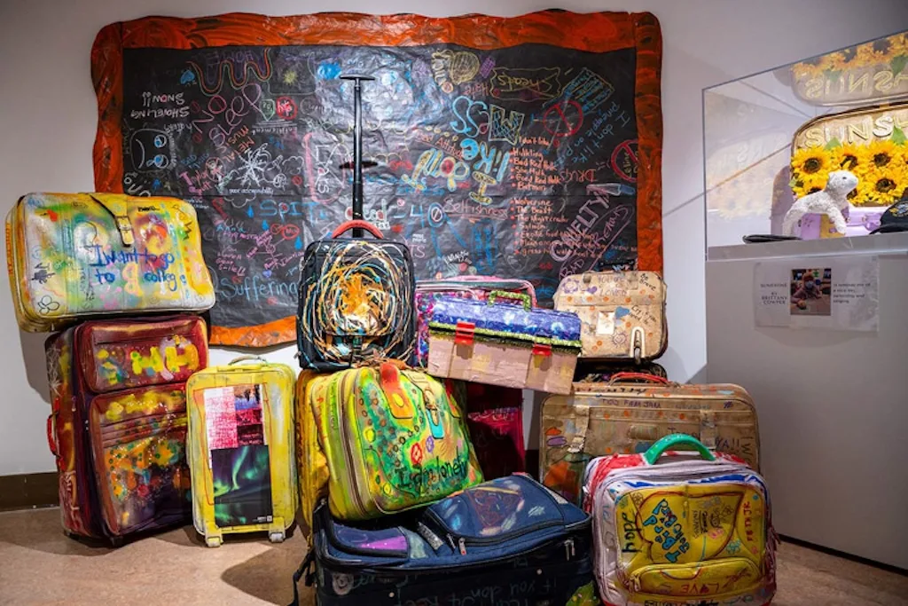 A colourful collection of decorated suitcases created by people at TOZ in 2022, with each suitcase representing individual stories and experiences