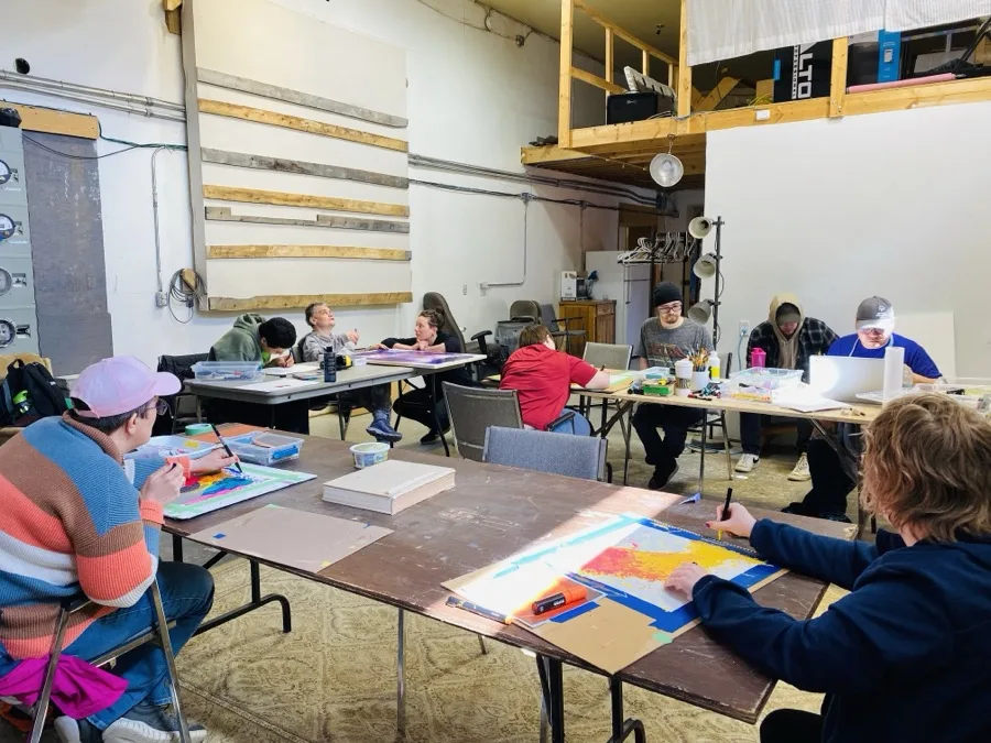 A group seated around tables creating colourful artwork together at the Warehouse, 2025