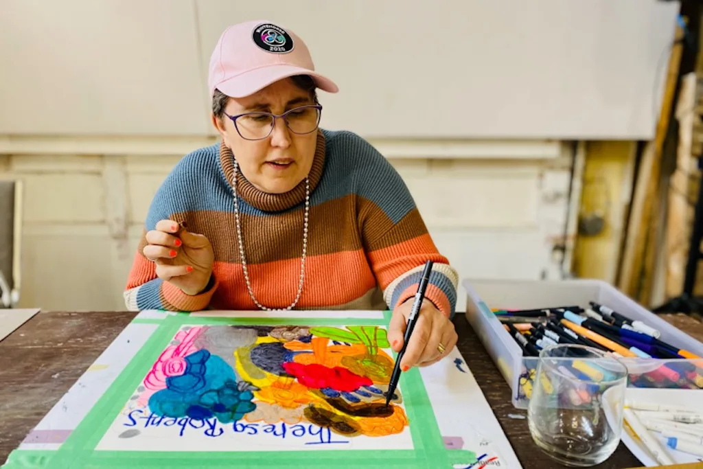 Theresa working on a colourful artwork with markers at the Warehouse, 2025