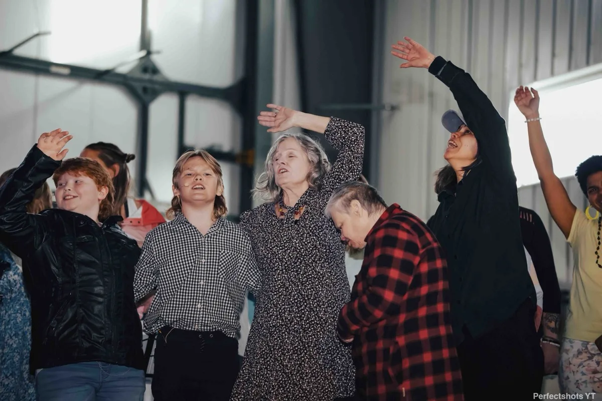 Group performing together with their arms raised during the Draw Us In film premiere and multimedia performance at Tintina Air hangar, 2023